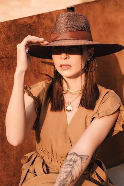 Moda joven mujer vestida con un vestido de verano con un sombrero ancho de mimbre camina y posa en la ciudad vieja.