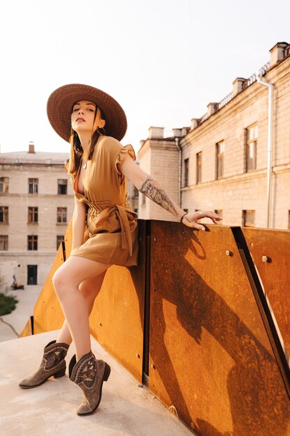 Moda joven mujer vestida con un vestido de verano con un sombrero ancho de mimbre camina y posa en la ciudad vieja.