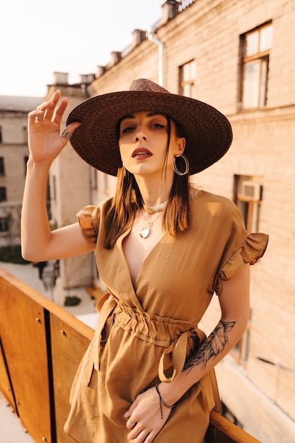 Moda joven mujer vestida con un vestido de verano con un sombrero ancho de mimbre camina y posa en la ciudad vieja.