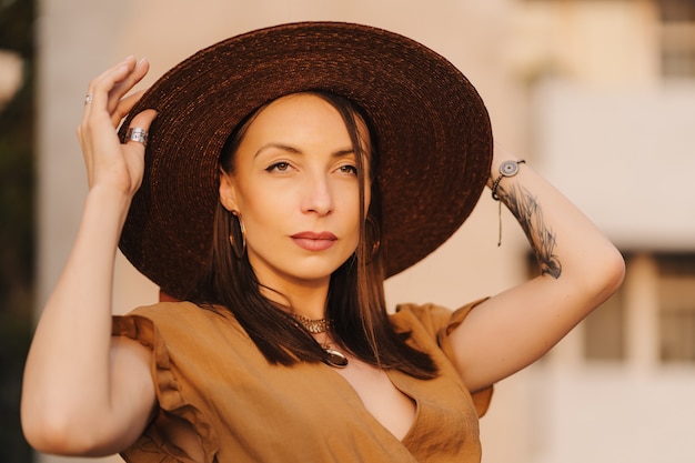 Moda joven mujer vestida con un vestido de verano con un sombrero ancho de mimbre camina y posa en la ciudad vieja.