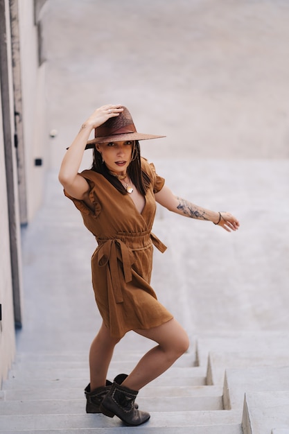 Moda joven mujer vestida con un vestido de verano con un sombrero ancho de mimbre camina y posa en la ciudad vieja.