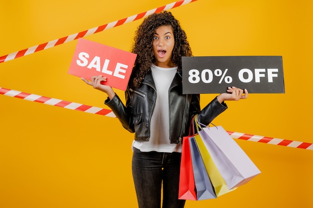 Moda joven negra con cartel de 80% de venta y coloridas bolsas de compras aisladas sobre amarillo con cinta de señal