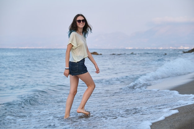 Moda joven con pelo largo teñido de azul caminando por la orilla del mar