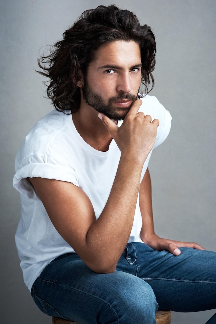 Foto moda legal e retrato de homem com confiança roupas de designer e relaxar em cadeira em estúdio jeans orgulho e casual modelo masculino em um banquinho com estilo criativo estética de moda ou fundo cinza