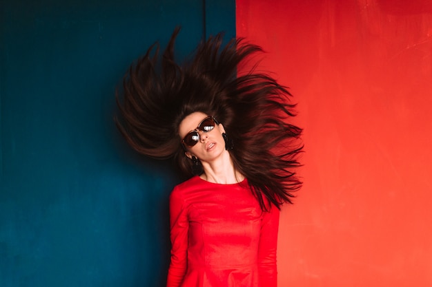 Moda linda mulher com cabelos longos escuros no vestido vermelho, posando na parede vermelha