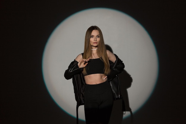 Moda moda mujer hermosa modelo hipster en elegante ropa de rock negro con top y chaqueta de cuero negro en estudio sobre un fondo oscuro