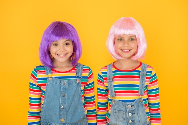 La moda moderna se crea para disfrutar Las niñas felices usan pelucas de cabello de moda fondo amarillo Los niños pequeños sonríen en un estilo de moda informal Moda elegante Salón de belleza y peluquería