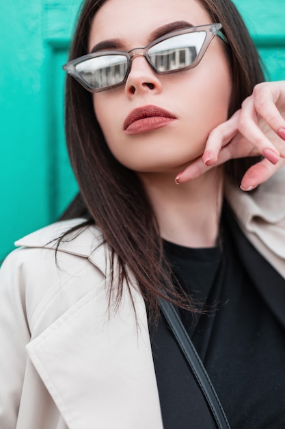 Foto moda moderna. retrato de mujer en gabardina de moda en blazer negro con camiseta elegante posando junto a la pared de madera turquesa en la calle. nueva colección de ropa de moda para mujer.