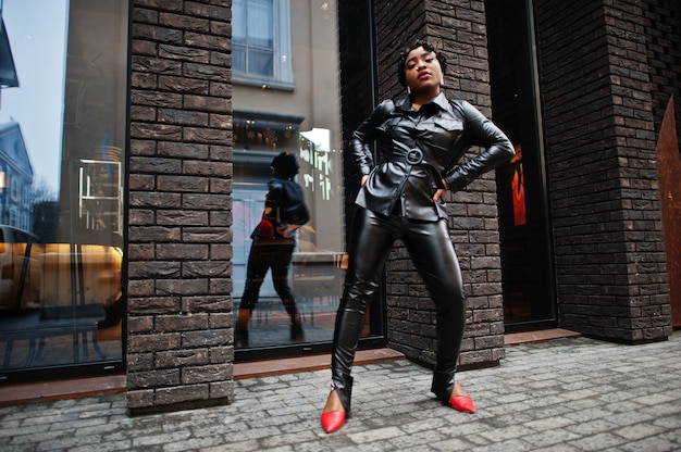 Moda mujer afroamericana hermosa posando en pantalones y chaqueta de cuero negro en la calle.