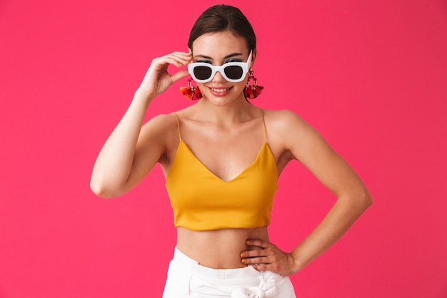 Moda mujer con aretes de moda tocando gafas de sol y sonriéndote