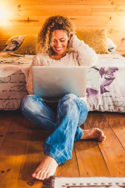 Moda mujer feliz alegre hermosa sentada en el piso de madera en casa u hotel con computadora portátil moderna conectada a internet