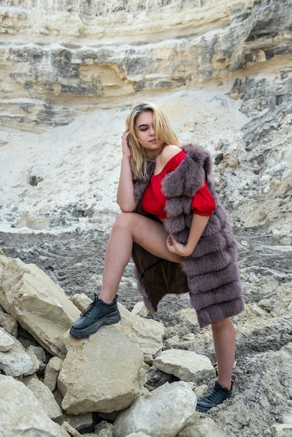 Moda mujer joven en abrigo de piel posando sobre rocas de arena