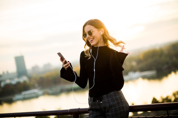 Moda mujer joven escuchando música desde el teléfono inteligente al aire libre al atardecer