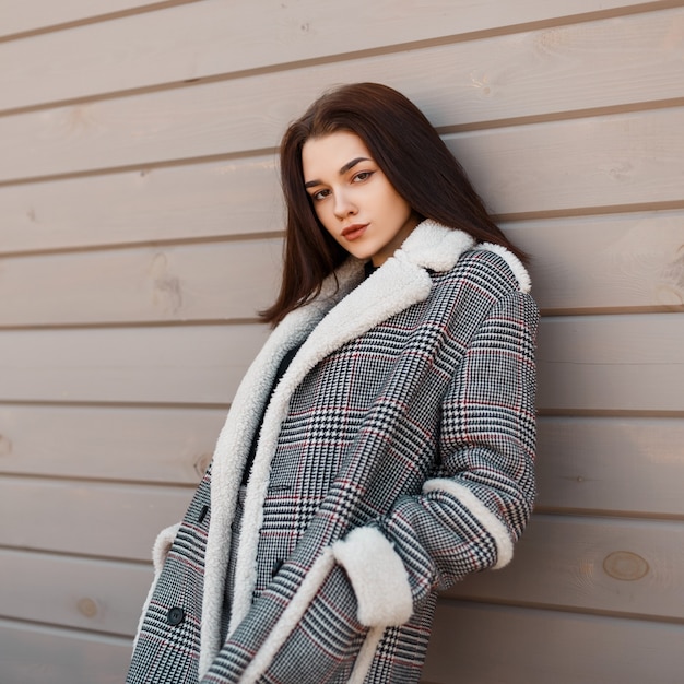 Moda mujer joven en ropa elegante con abrigo vintage se encuentra ordenado sobre un fondo de madera