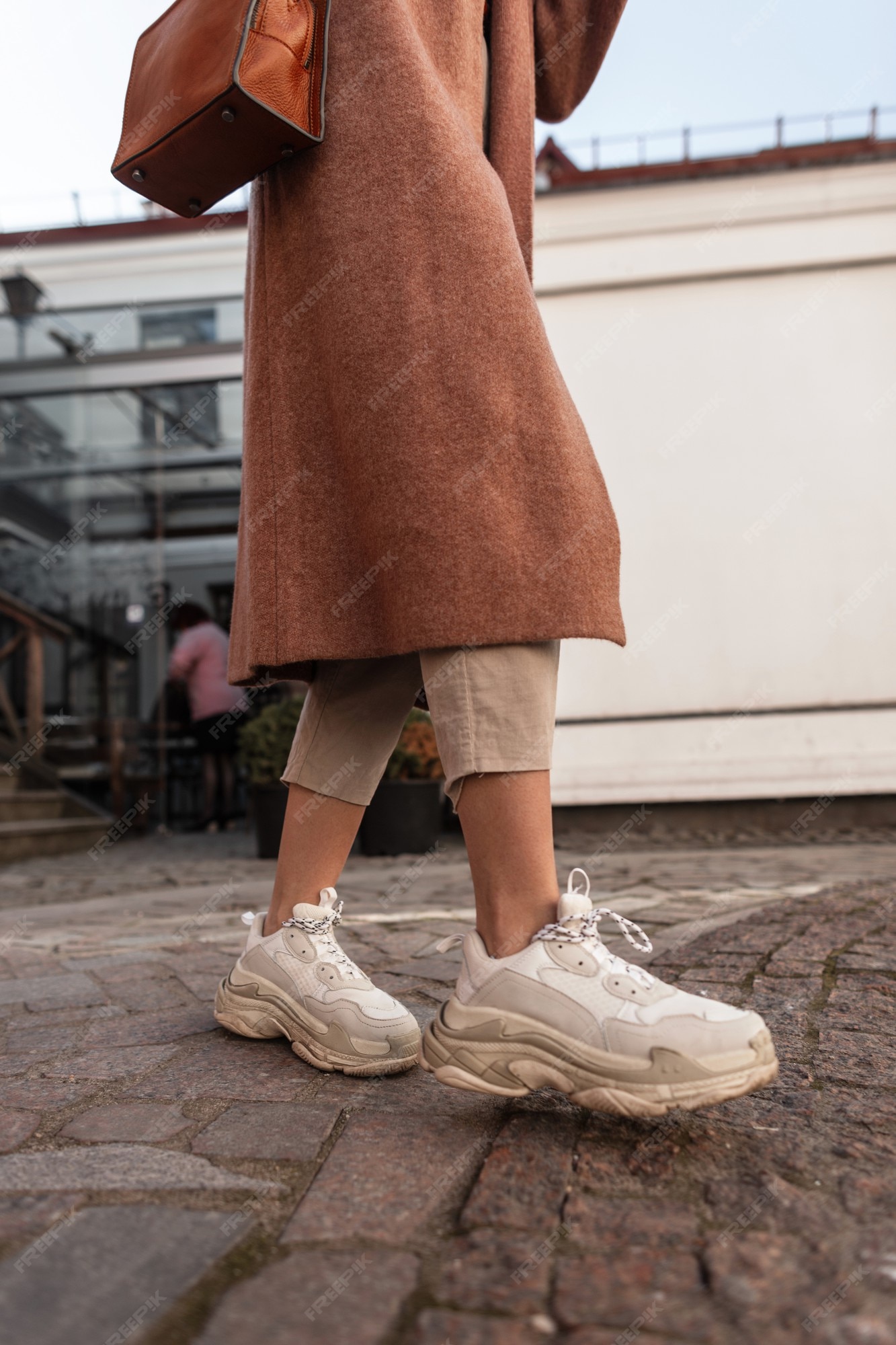 Moda mujer moderna en abrigo largo y elegante con bolso de cuero marrón en zapatillas con estilo se en el piedra. cerrar las femeninas con ropa de moda