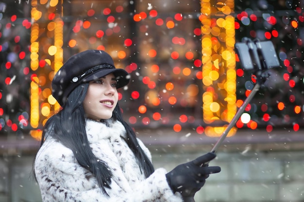 Moda mujer morena con cabello largo tomando selfie en su teléfono inteligente en la feria de Navidad. Espacio para texto