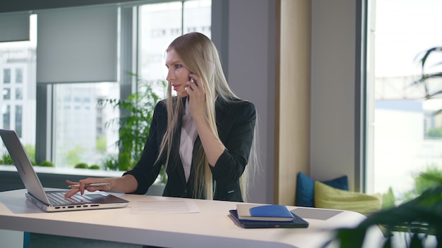 Moda mujer de negocios mirando portátil y hablando por teléfono.