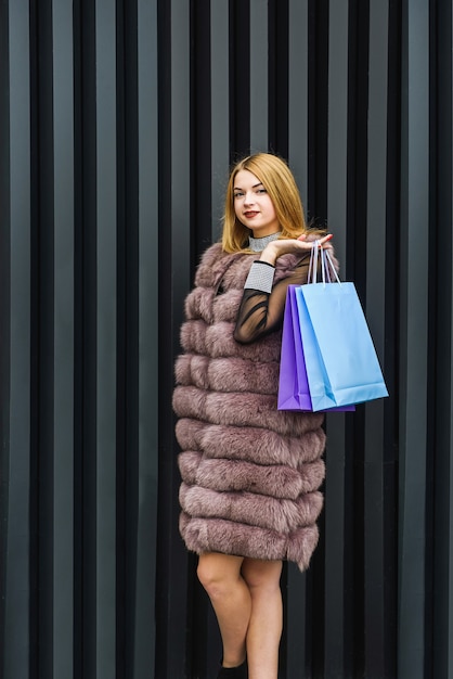 Moda mulher em vestido preto e casaco de pele posando com sacolas de compras ao ar livre