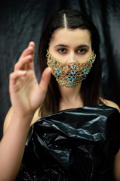 Moda pandémica Accesorio de cuarentena Fiesta de disfraces Nueva normalidad Mujer misteriosa en cadena de oro de lujo máscara facial polietileno negro aislado sobre fondo oscuro