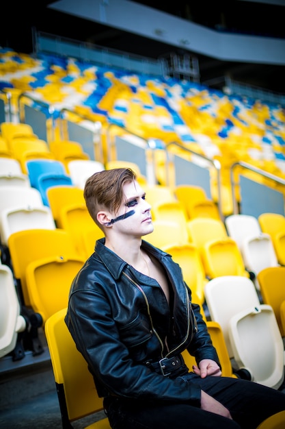 Moda relajada para hombres con chaqueta de cuero posando mientras están sentados en el estadio