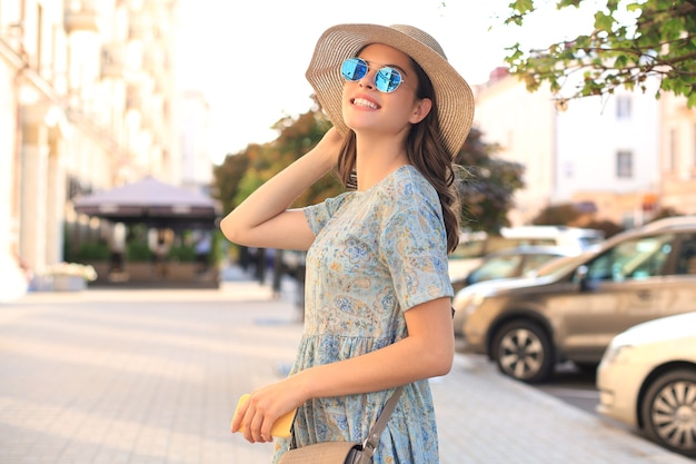 Moda retrato mulher em vestido azul em óculos de sol, andando na rua e segurando o smartphone na mão.
