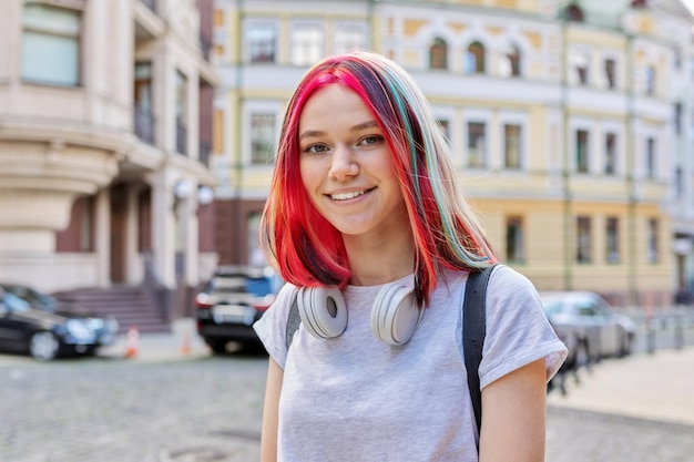 Moda sonriente feliz hermosa niña adolescente 16 17 años con auriculares inalámbricos con peinado de color teñido brillante en la calle de la ciudad soleada de verano Belleza de moda juvenil de estilo de vida