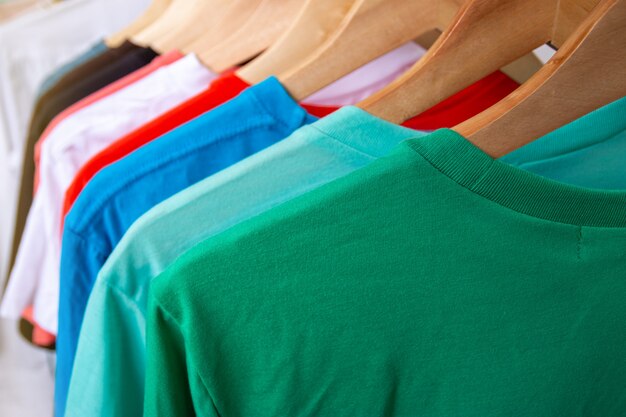 Foto moda t-shirt no cesto de roupas - close-up do armário colorido brilhante em cabides de madeira no armário da loja.