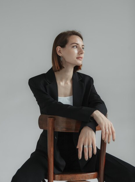 Mode-Aufnahme einer jungen stilvollen Frau in schwarzem Anzug, die im Studio auf einem Stuhl sitzt