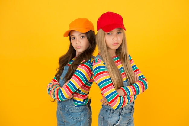 Mode, die zu ihrem bewussten Stil passt Kleine Mädchen mit Stil, die Arme auf gelbem Hintergrund verschränkt halten Kleine Kinder mit Baseballmützen im lässigen Streetwear-Stil Hip-Hop- oder Hipster-Stil