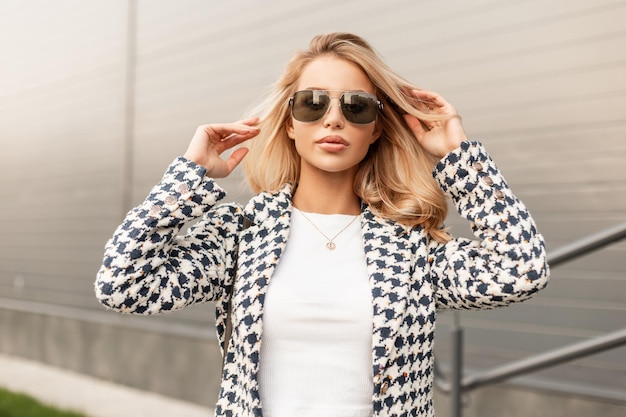 Mode elegantes blondes Frauenmodell mit stylischer Sonnenbrille in Luxus-Outwear auf der Straße