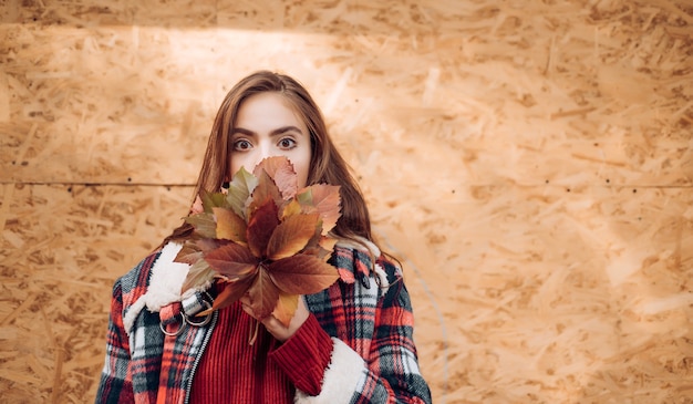 Mode-Herbstporträtfrau mit gelben Ahornblättern auf gelbem hölzernem Hintergrund