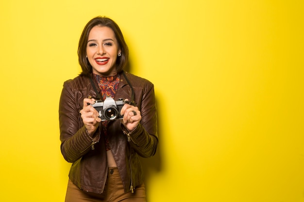 Mode junge Frau macht das Foto mit alter Kamera auf gelber Wand