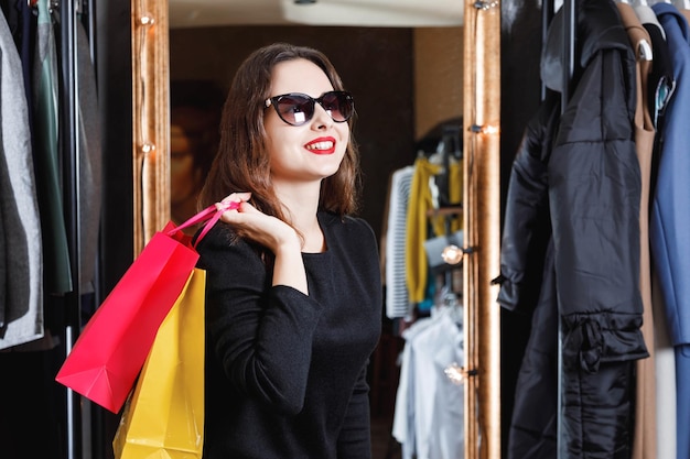 Mode junges brünettes Haarmädchen mit Sonnenbrille, das an ein neues Kleid im Konzept des schwarzen Freitags des Einkaufszentrums denkt