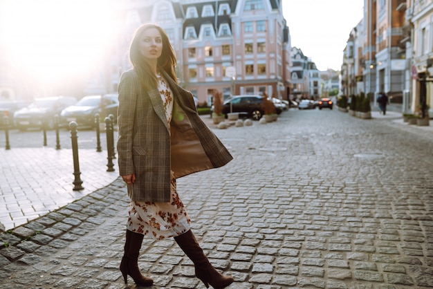 Mode-Lebensstil-Porträt der jungen glücklichen hübschen Frau, die auf der Straße bei Sonnenuntergang geht. Stilvolles und elegantes Mädchen.