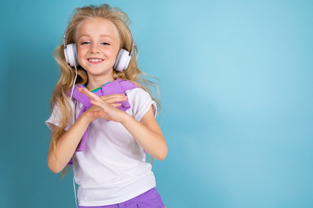 Mode Mädchen Blondine mit langen Haaren in Sporthemd, Shorts, Turnschuhe stehen, hören Musik mit Kopfhörern, Tänzen und Lächeln