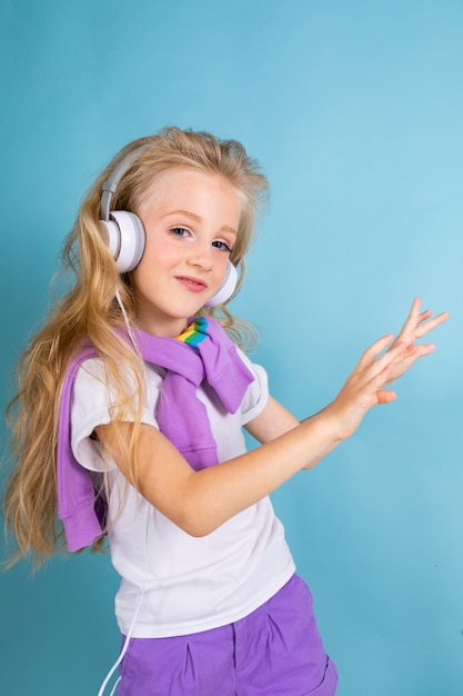 Mode Mädchen Blondine mit langen Haaren in Sporthemd, Shorts, Turnschuhe stehen, hören Musik mit Kopfhörern und Tänzen