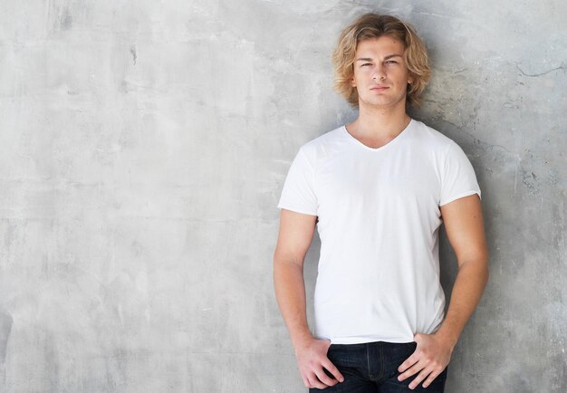 Foto mode-modell des jungen mannes, das im weißen t-shirt auf wandhintergrund aufwirft