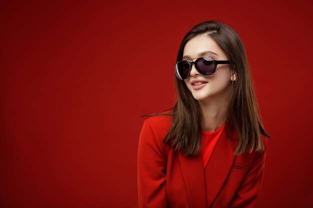 Mode-Modell in roter Anzugjacke Rock Sonnenbrille Schöne junge Frau Roter Hintergrund