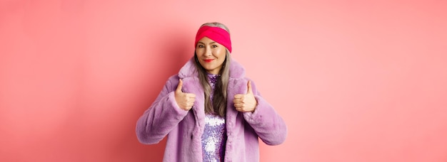 Foto mode- und einkaufskonzept asiatische modische dame im wintermantel, die daumen hoch lächelnd und aussehen zeigt
