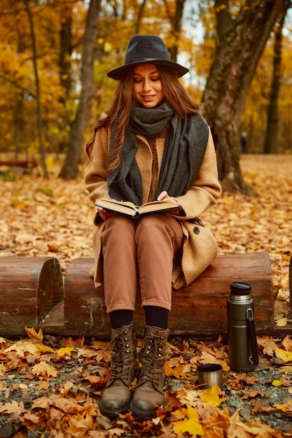 Mode wunderschöne Frau Rest Lesebuch im Wald sitzt auf Baumstamm mit Tee in Thermoskanne. Herbstspaziergang