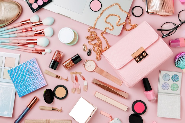 Modeblogger-Arbeitsplatz mit Laptop und weiblichen Accessoires-Kosmetikprodukten auf blassrosa Tisch