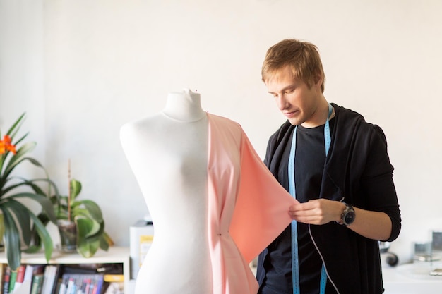 Foto modedesigner mit einem dummy, der im studio kleid macht