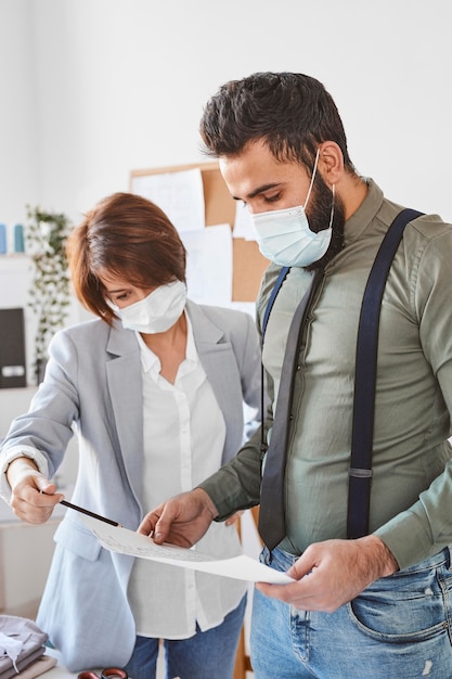 Modedesigner mit medizinischen Masken überprüfen die Pläne der Modelinie im Atelier