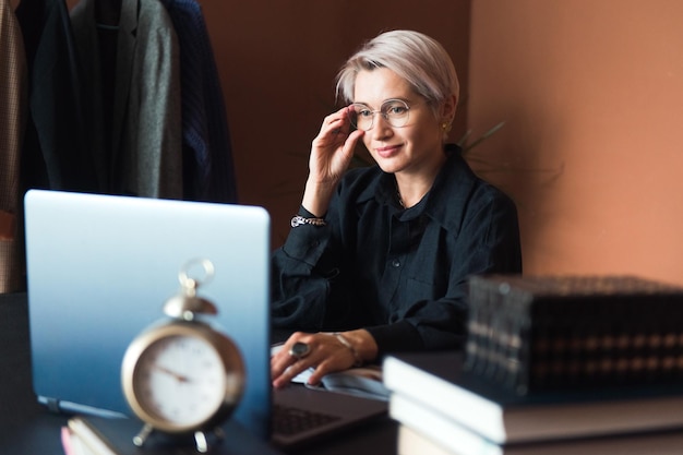 Modefrau im schwarzen Hemd, die an einem modernen Arbeitsplatz oder im Büro mit Laptop arbeitet