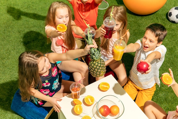 Modekonzept für Kinder. Die Gruppe von jugendlichen Jungen und Mädchen, die auf grünem Gras im Park sitzen. Bunte Kinderkleidung, Lifestyle, trendige Farbkonzepte.