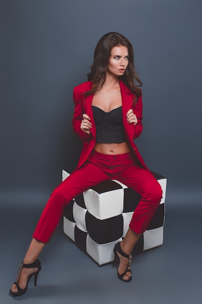 Model im roten Anzug. Junge Frau, die mit rotem Anzug auf Grau aufwirft
