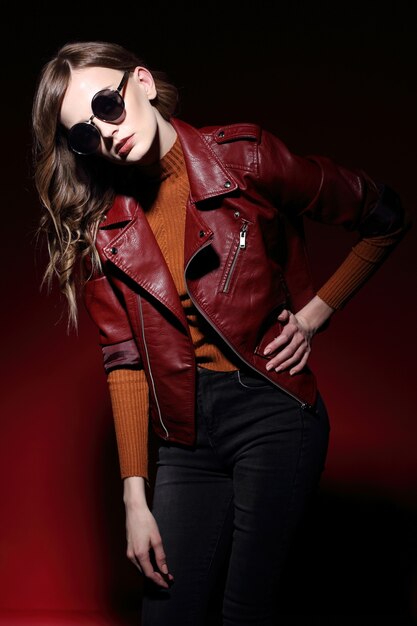 Model in Sonnenbrille, schöne junge Frau. Lederjacke, Studioaufnahme, roter Hintergrund