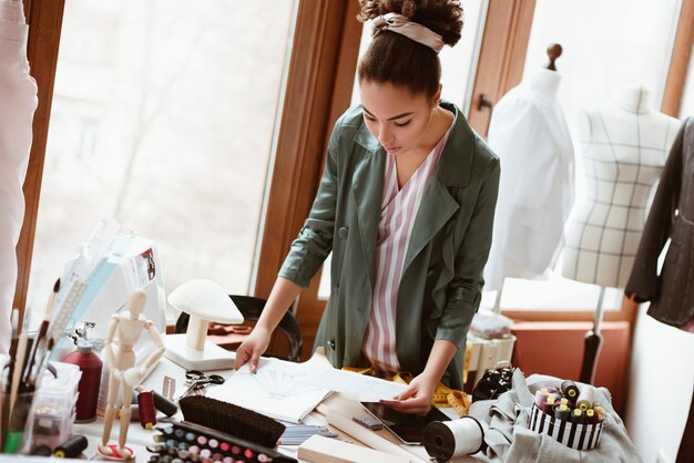 Modelado de nuevo diseño en not pad. Sastre de mujer joven sin bloc y lápiz está modelando ropa nueva en el estudio de diseño