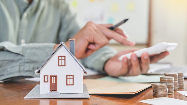 Modele casas y monedas con personas que usan la calculadora, concepto de costo de la casa.