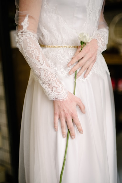 Modell, das in einem weißen Hochzeitskleid aufwirft, hält eine Blume in ihrer Hand